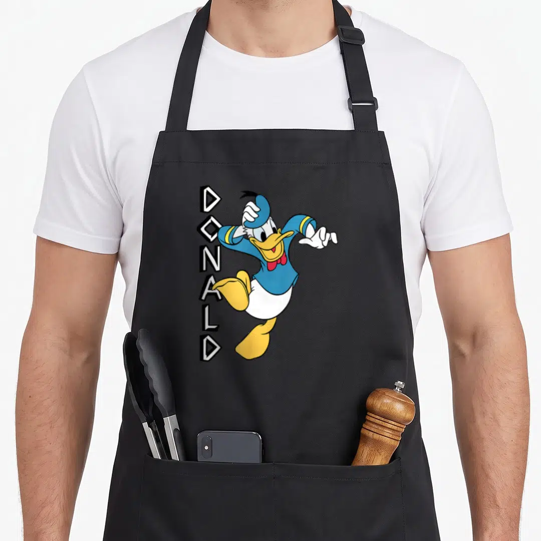 Jumping duck apron - Cartoon duck in blue yellow white and red with vertical DONALD text — shown on a black cotton canvas apron against a white background