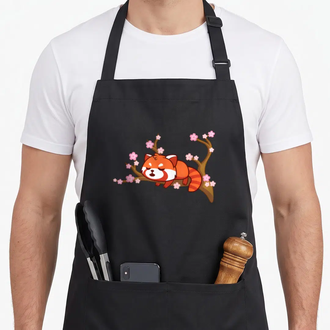 Panda cherry apron - Cartoon red panda sleeping on brown branch with pink cherry blossoms — shown on a black cotton canvas apron against a white background