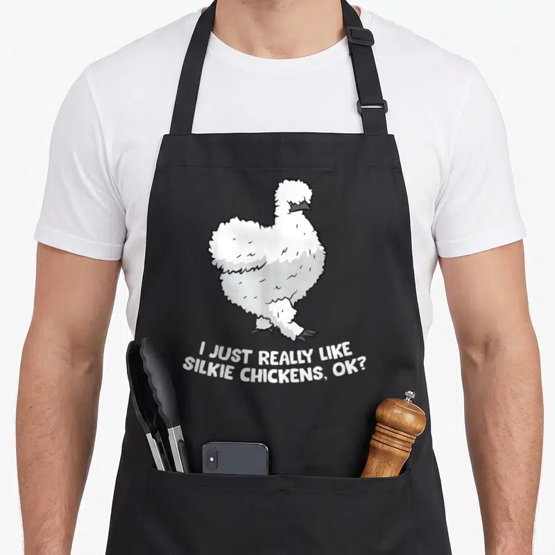 Funny silkie chicken apron - Cartoon white silkie chicken above stacked text I JUST REALLY LIKE SILKIE CHICKENS OK — shown on a black cotton canvas apron against a white background