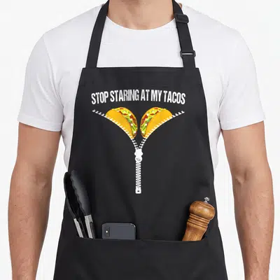 Stop mexican apron - Arched text above white zipper opening to show two tacos with yellow green and red fillings — shown on a black cotton canvas apron against a white background