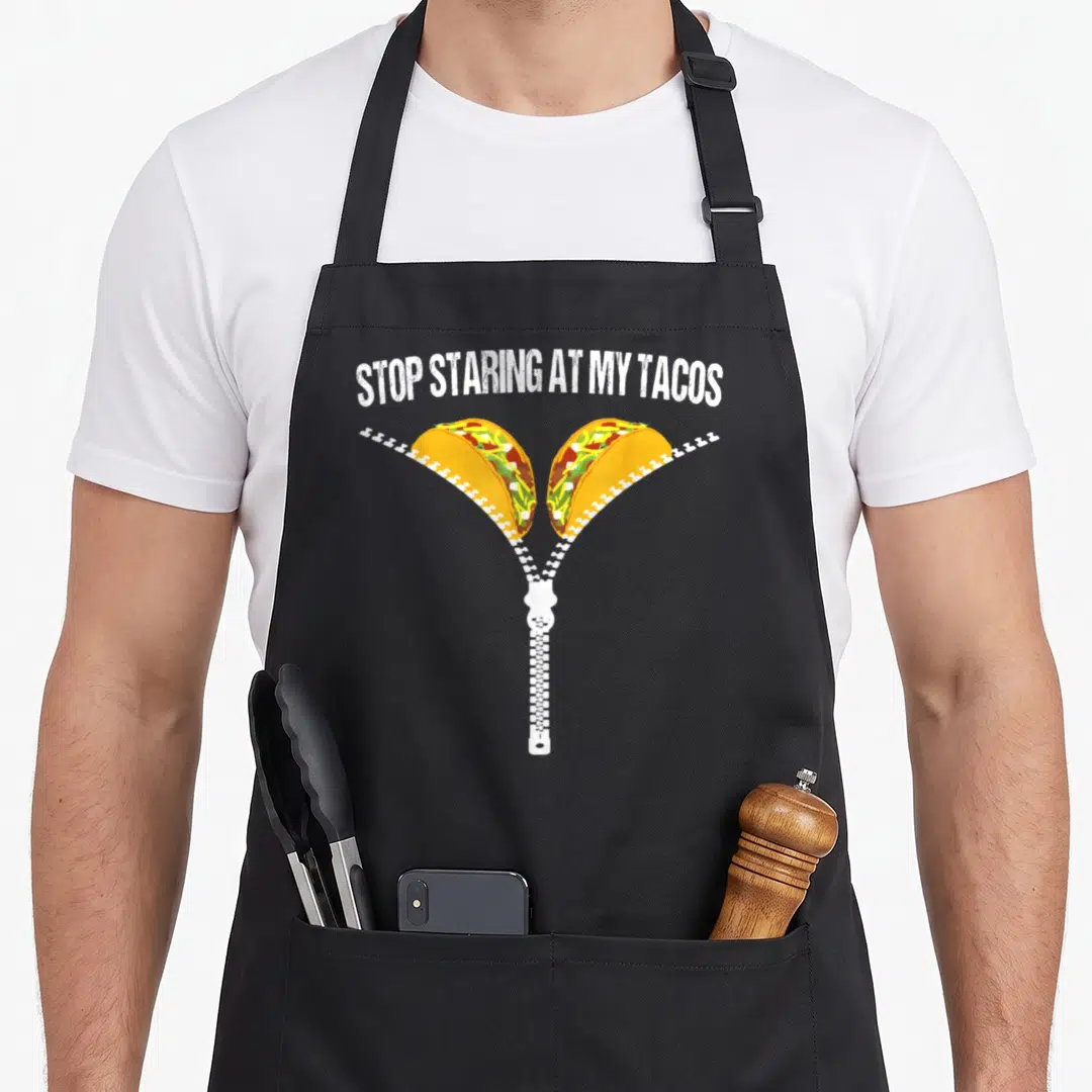 Stop mexican apron - Arched text above white zipper opening to show two tacos with yellow green and red fillings — shown on a black cotton canvas apron against a white background