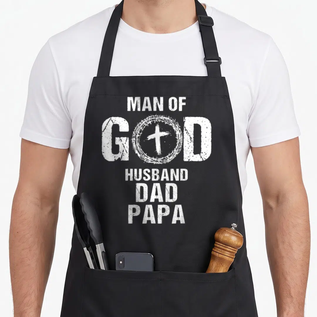 Husband papa father day apron - White distressed text MAN OF GOD HUSBAND DAD PAPA with cross inside crown of thorns — shown on a black cotton canvas apron against a white background