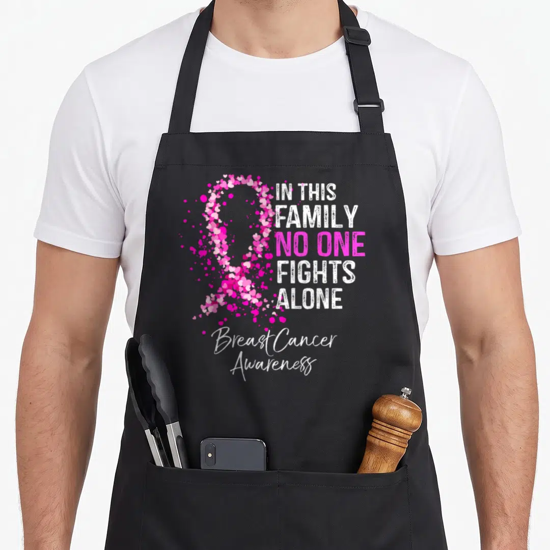 Family breast cancer awareness aprons - Pink ribbon formed by small hearts next to white and pink text reading IN THIS — shown on a black cotton canvas apron against a white background