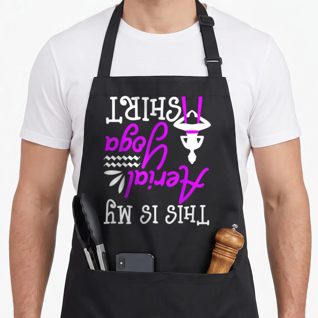 Aerial grill instructor apron - Vertical white and purple THIS IS MY AERIAL YOGA SHIRT text with inverted figure — shown on a black cotton canvas apron against a white background