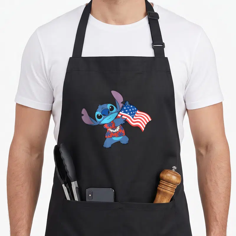 Stitch tropical print aprons - Blue cartoon character in red floral shirt holding USA flag with white lei — shown on a black cotton canvas apron against a white background
