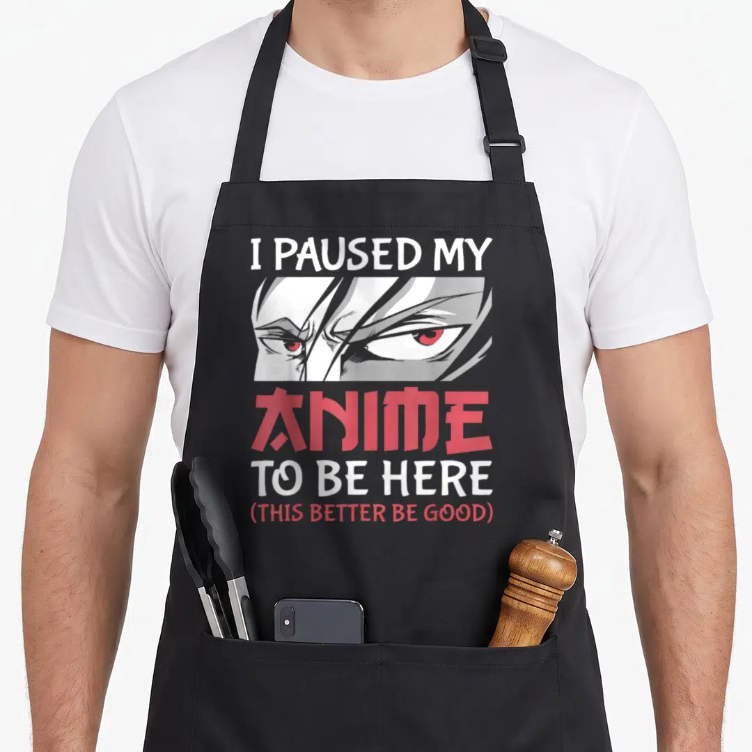 Paused japanese anime apron - I PAUSED MY ANIME TO BE HERE text with red anime eyes and Japanese katakana characters — shown on a black cotton canvas apron against a white background