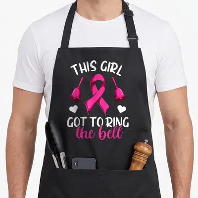 End bell apron - Pink awareness ribbon flanked by two bells and hearts with celebratory text — shown on a black cotton canvas apron against a white background