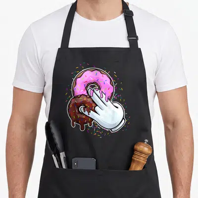 Funny stink the dirty apron - White gloved hand dipping into pink and brown frosted donuts with scattered sprinkles — shown on a black cotton canvas apron against a white background