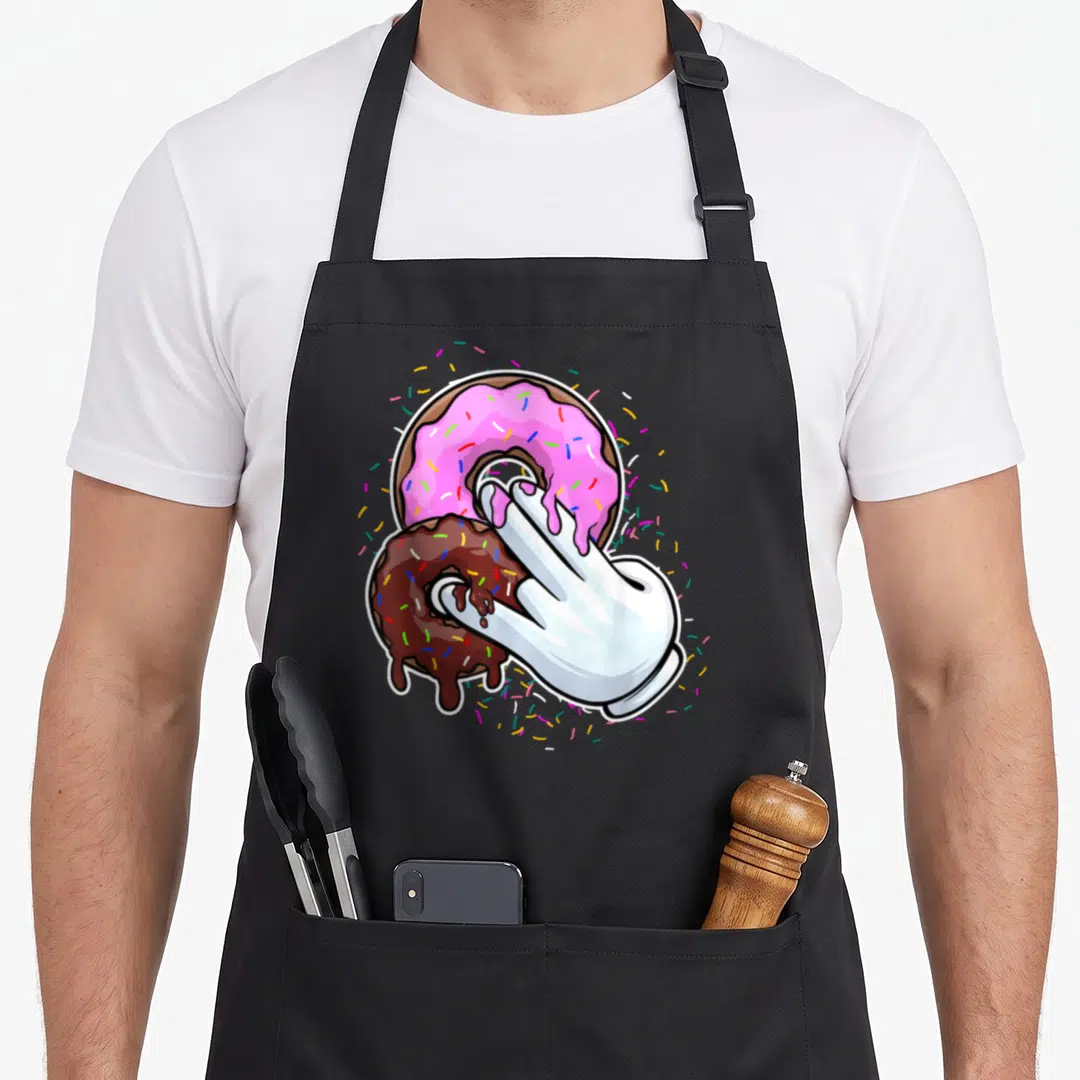 Funny stink the dirty apron - White gloved hand dipping into pink and brown frosted donuts with scattered sprinkles — shown on a black cotton canvas apron against a white background