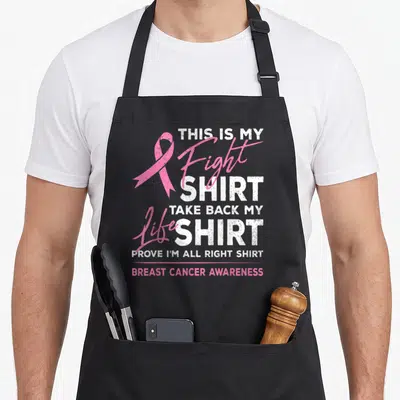 Fight breast ribbon apron - Pink awareness ribbon next to distressed white and pink text reading This Is My Fight Shirt — shown on a black cotton canvas apron against a white background