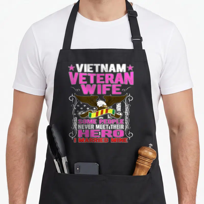 Their wife apron - Eagle holding striped ribbon with Vietnam Veteran Wife text and pink distressed lettering — shown on a black cotton canvas apron against a white background