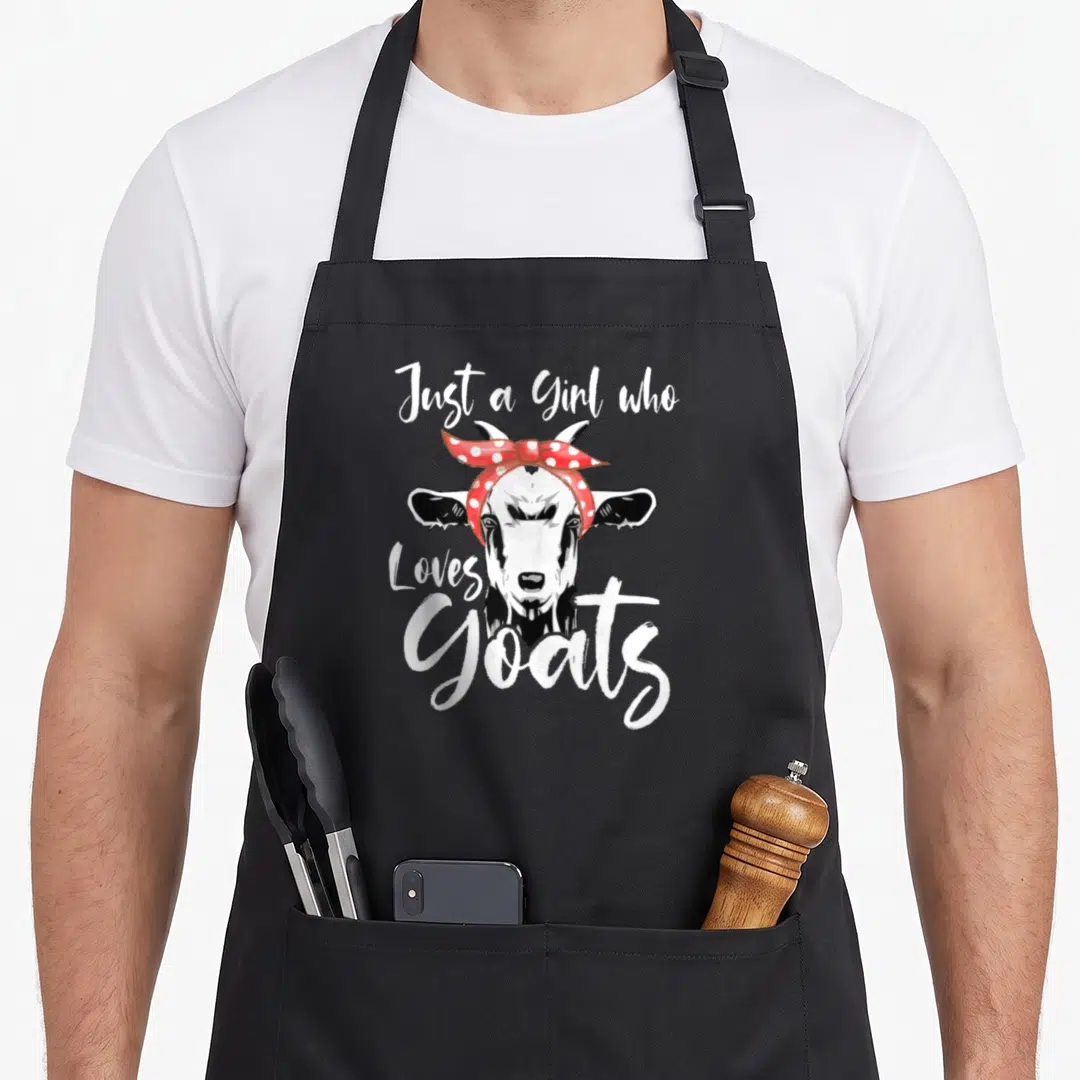 Cute goat aprons - Cartoon goat head wearing red polka dot bandana with white text Just a Girl who Loves Goats — shown on a black cotton canvas apron against a white background