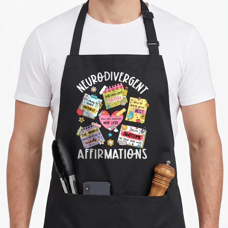 Neurodiversity neurologist apron - Neuro-divergent affirmation notes, rainbow heart, and school supplies in white — shown on a black cotton canvas apron against a white background