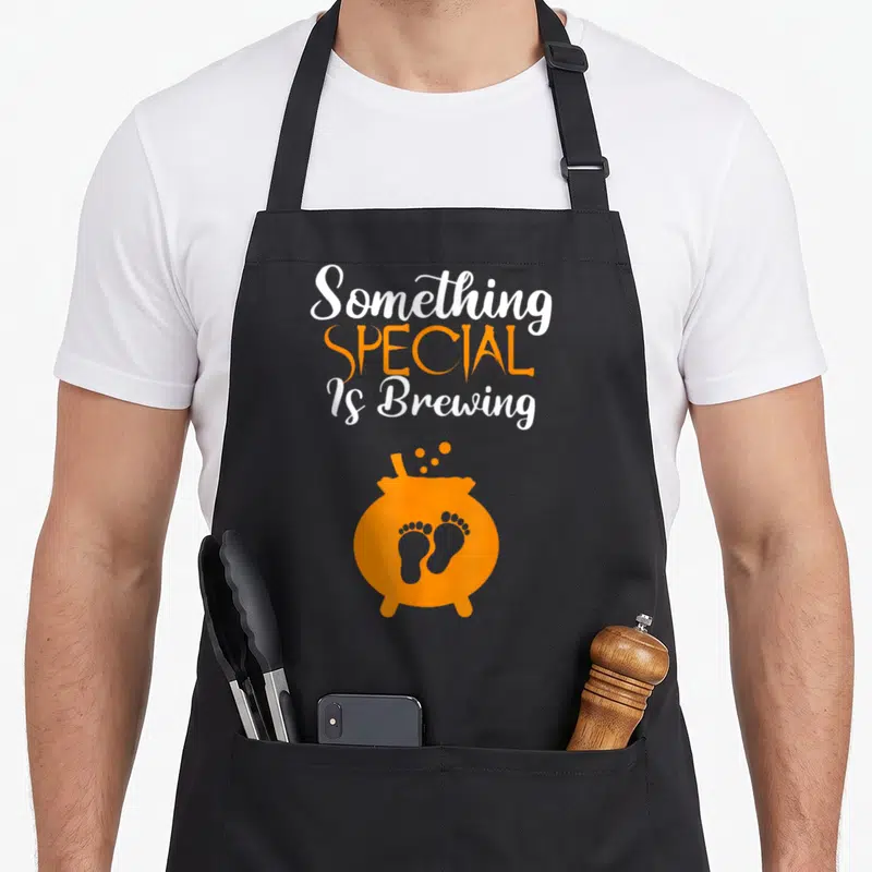 Special halloween apron - Orange cauldron with two footprints and text Something SPECIAL Is Brewing — shown on a black cotton canvas apron against a white background