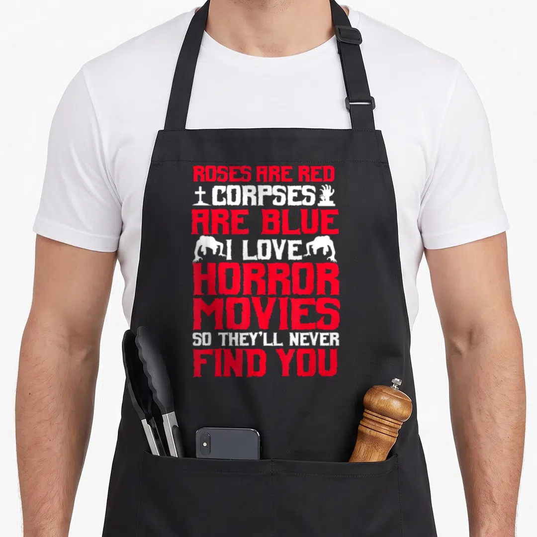 Movy halloween apron - Roses Are Red Corpses Are Blue text with zombie hands and gravestone in red and white — shown on a black cotton canvas apron against a white background