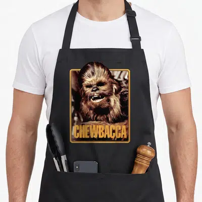 Funny trading cards apron - Photo of Chewbacca in gold frame with CHEWBACCA text in brown and black — shown on a black cotton canvas apron against a white background
