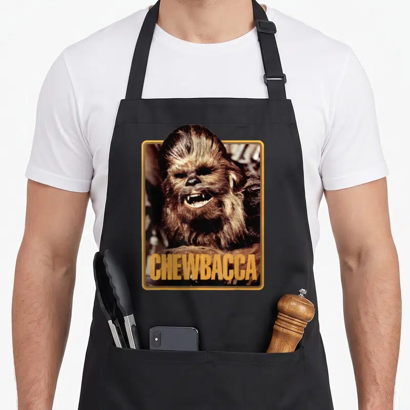 Funny trading cards apron - Photo of Chewbacca in gold frame with CHEWBACCA text in brown and black — shown on a black cotton canvas apron against a white background