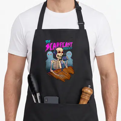 Scarecrow horror apron - Skeleton with headphones holding mug at mic with The Scarecast Podcast text — shown on a black cotton canvas apron against a white background