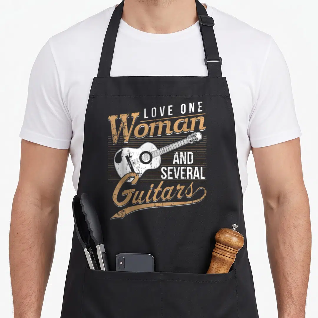 Guitarist songwriter apron - Retro tan and white text reading Love One Woman And Several Guitars around an acoustic — shown on a black cotton canvas apron against a white background