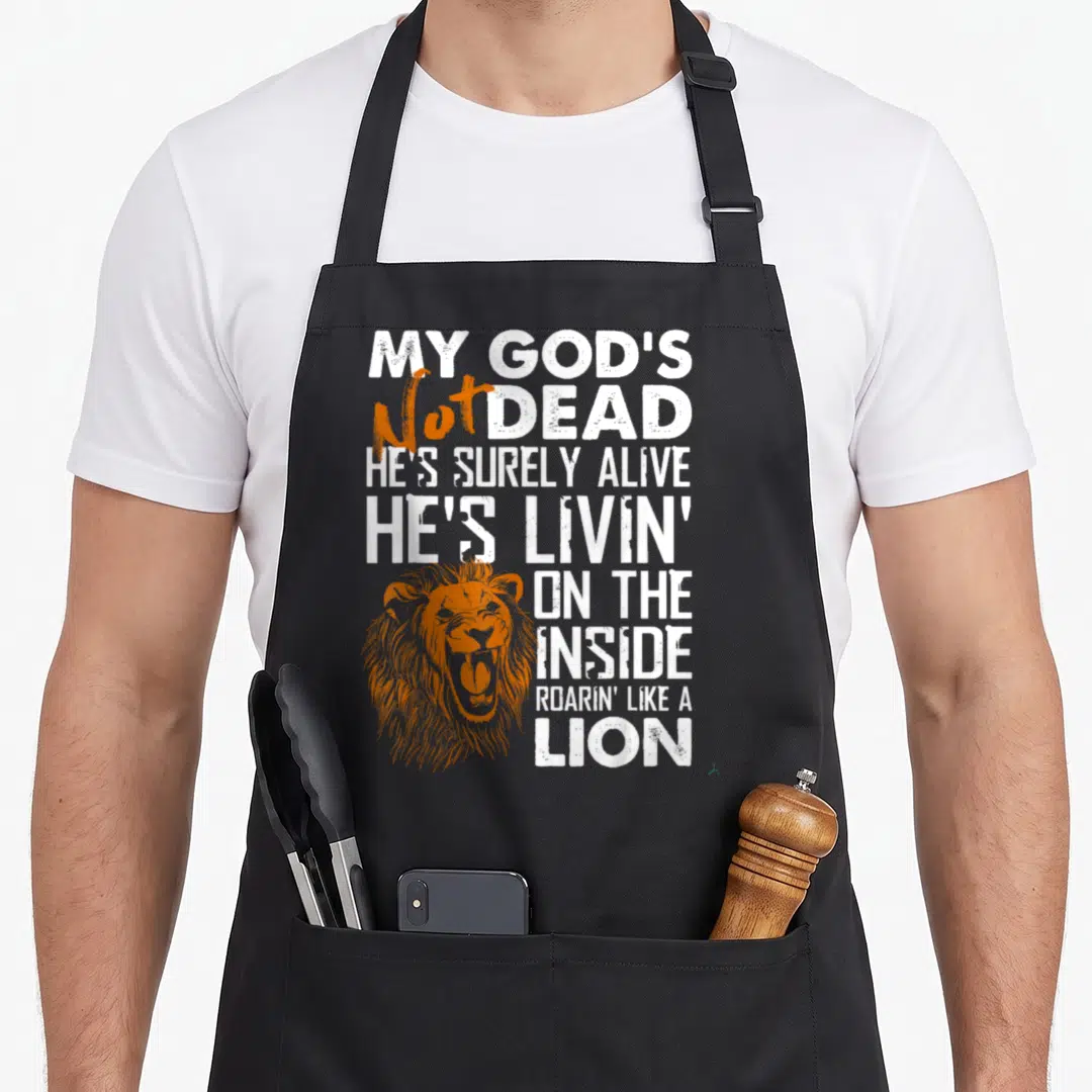 Dead cross apron - My God's Not Dead text stacked with orange lion head overlapping bottom left corner — shown on a black cotton canvas apron against a white background