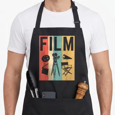 Film maker apron - Grey FILM text over red beige teal yellow stripes with camera reel clapperboard chair megaphone — shown on a black cotton canvas apron against a white background