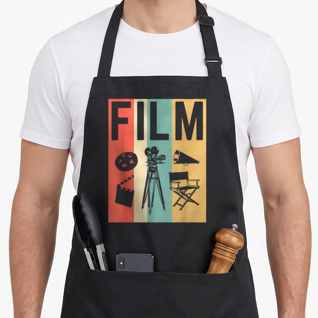 Film maker apron - Grey FILM text over red beige teal yellow stripes with camera reel clapperboard chair megaphone — shown on a black cotton canvas apron against a white background