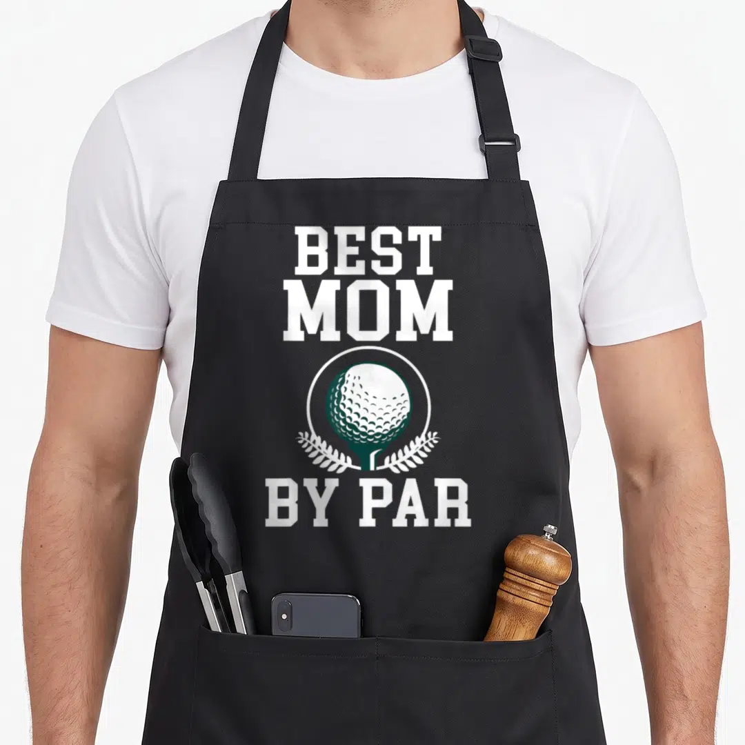 Par golfing mother golf apron - BEST MOM BY PAR text with white and green golf ball on tee inside circle — shown on a black cotton canvas apron against a white background
