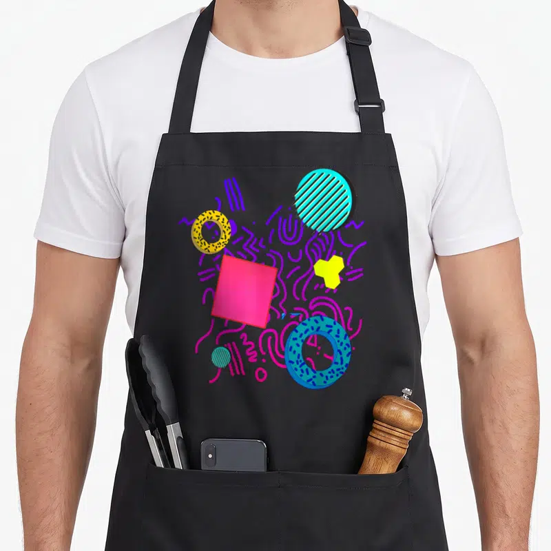 Geometric memphis apron - Abstract pink square, striped teal circle, and dotted donuts in purple, pink, yellow, blue — shown on a black cotton canvas apron against a white background