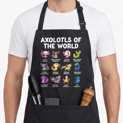 Animal kawaii apron - Twelve cartoon axolotls in a grid with labels like Wild Brown, Albino, Silver Dalmatian, and GFP — shown on a black cotton canvas apron against a white background