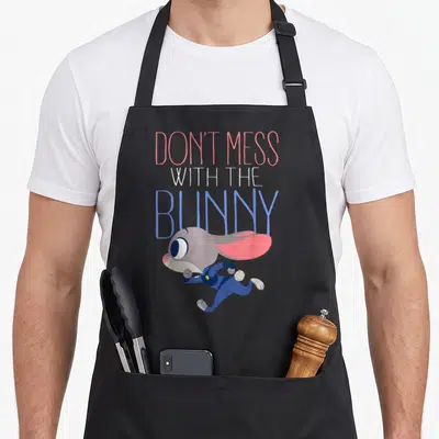 Mess novelty apron - Stacked text Don't Mess With The Bunny above a running grey cartoon bunny in pink and blue — shown on a black cotton canvas apron against a white background