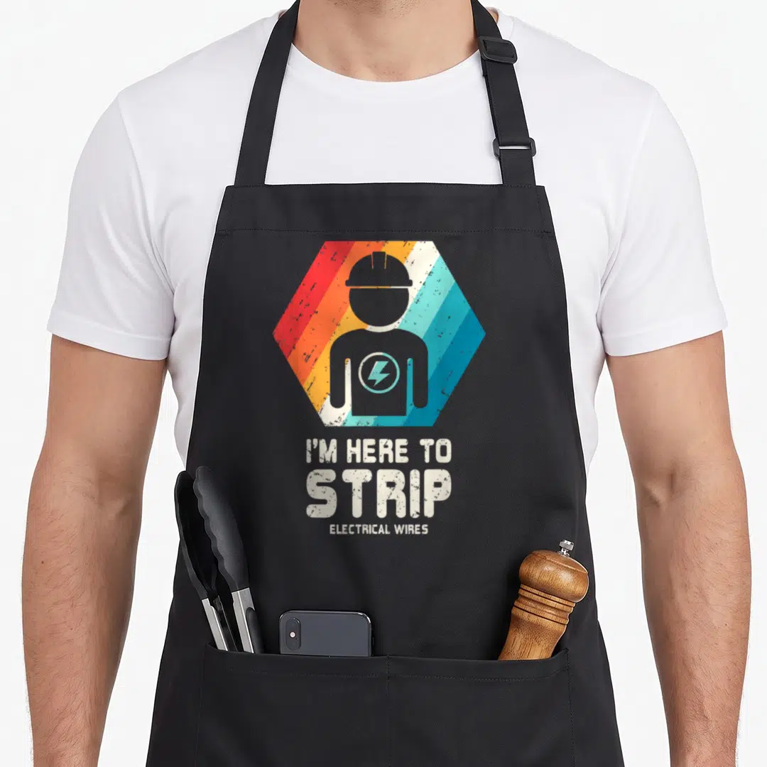 Husband electricians apron - Grey electrician silhouette in red orange blue striped hexagon with text I M HERE TO STRIP — shown on a black cotton canvas apron against a white background
