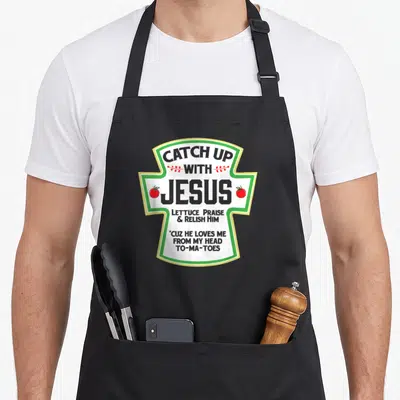 Funny christian catch up with jesus apron - Ketchup label design with two red tomatoes and text catching up with jesus — shown on a black cotton canvas apron against a white background