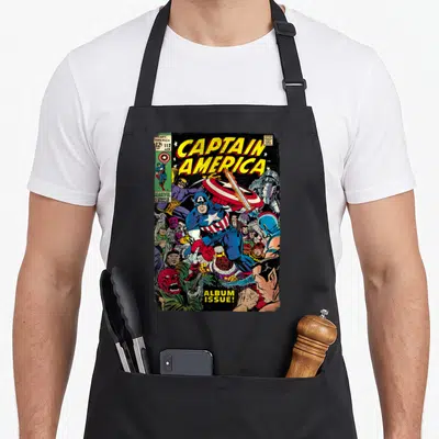 Villain captain apron - Captain America comic cover with villains, yellow title text, and red blue colors — shown on a black cotton canvas apron against a white background