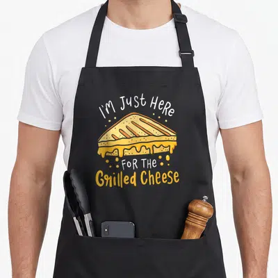 Grilled cheese apron - Cartoon grilled cheese sandwich with melting yellow cheese and white and orange text reading I'm — shown on a black cotton canvas apron against a white background