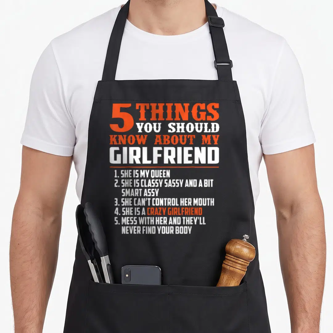 Funny should girlfriend funny apron - Orange and white typography listing 5 things you should know about my girlfriend — shown on a black cotton canvas apron against a white background