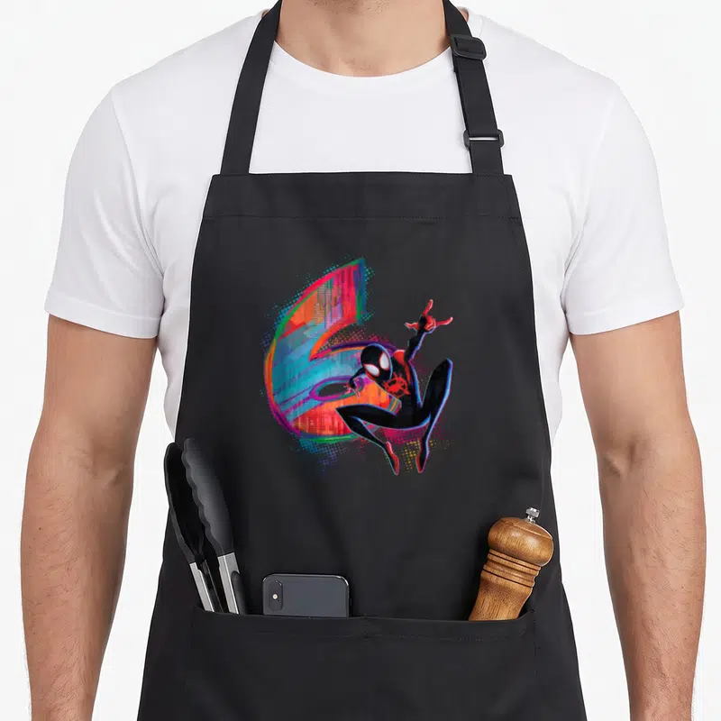 Morale 6th birthday apron - Miles Morales crouching before large multicolored number 6 with halftone dots — shown on a black cotton canvas apron against a white background