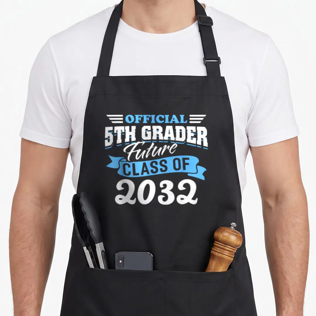 5th gabep0s apron - OFFICIAL 5TH GRADER Future CLASS OF 2032 text design with wings and ribbon — shown on a black cotton canvas apron against a white background