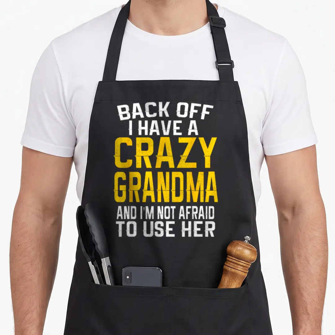 Retro grandmother grandma apron - White and yellow distressed text reading BACK OFF I HAVE A CRAZY GRANDMA AND I'M NOT — shown on a black cotton canvas apron against a white background