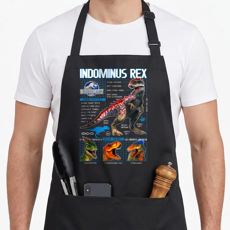 Indominus t-rex apron - Indominus Rex schematic with stats, three enemy heads, and blue grid lines — shown on a black cotton canvas apron against a white background