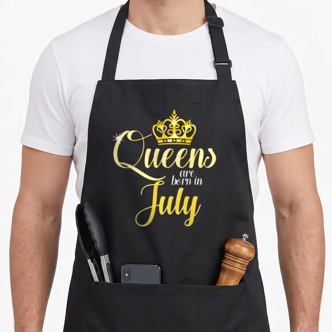 Date birthday apron - Yellow crown and script text reading Queens are born in July — shown on a black cotton canvas apron against a white background