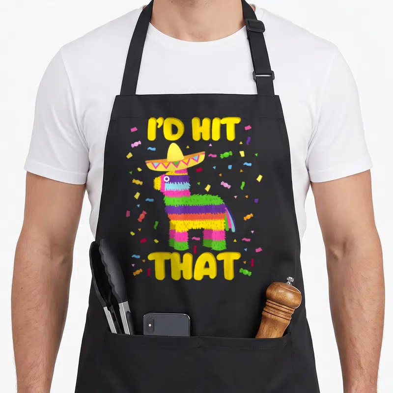 Hit cinco de mayo apron - I'D HIT THAT text around a striped piñata with sombrero and scattered candy confetti — shown on a black cotton canvas apron against a white background