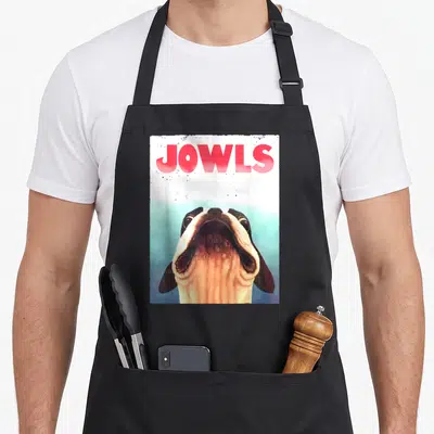 Jowl dog apron - Red JOWLS text above a realistic dog head looking upward on white and blue background — shown on a black cotton canvas apron against a white background