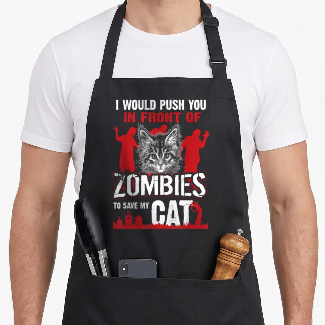 Would cat apron - Distressed text I Would Push You in Front of Zombies to Save My Cat with grey cat head and red — shown on a black cotton canvas apron against a white background