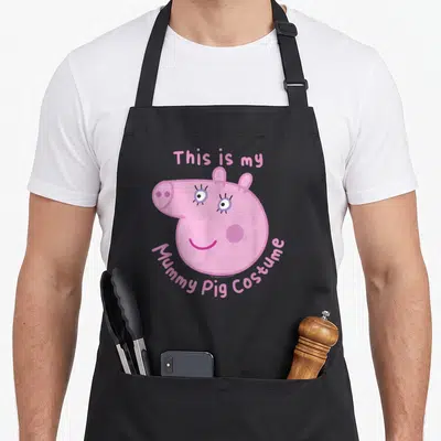 Funny halloween mummy and me aprons - Pink pig face with arched text This is my Mummy Pig Costume in cartoon style — shown on a black cotton canvas apron against a white background
