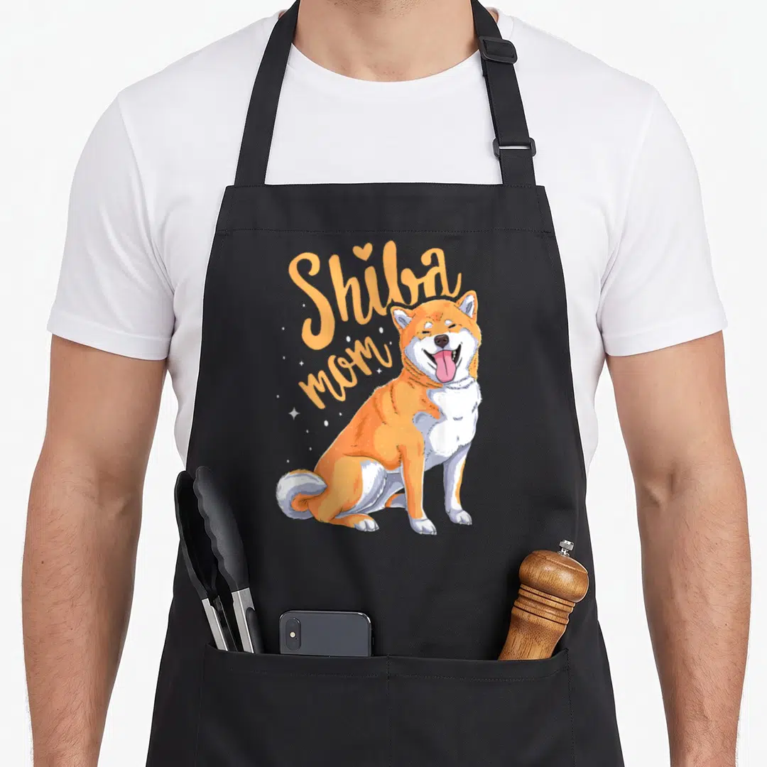 Inu mama dog apron - Cartoon sitting Shiba Inu in orange and white next to Shiba mom text with stars and heart — shown on a black cotton canvas apron against a white background