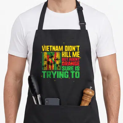 Vietnam retired veteran apron - Distressed text Vietnam didn't kill me with helicopter and palm tree graphic in yellow — shown on a black cotton canvas apron against a white background