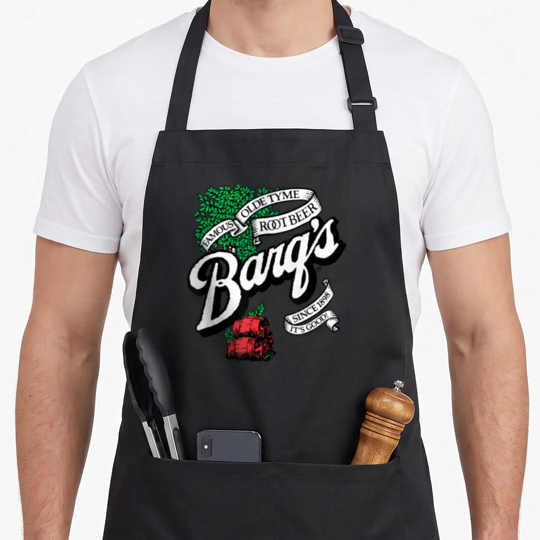 Coca beer apron - Retro Barq's Root Beer logo with ribbons, green leaves, and red barrels on white background — shown on a black cotton canvas apron against a white background