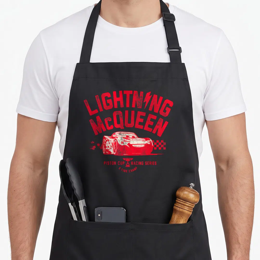 Badge car apron - Red distressed race car with arched text PISTON CUP RACING SERIES 5 TIME CHAMP and checkered flag — shown on a black cotton canvas apron against a white background