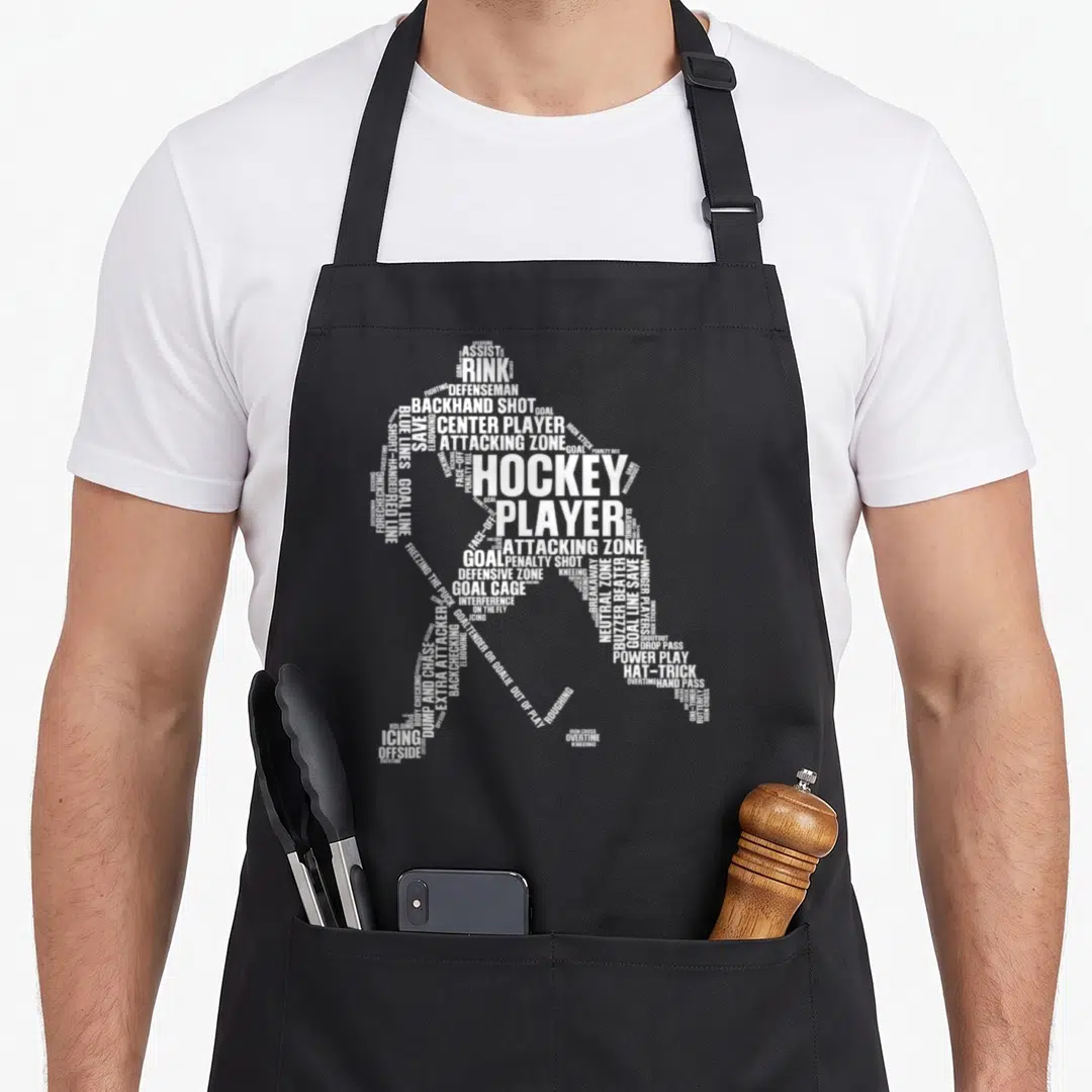 Cute player hockey ice apron - White typography silhouette of a hockey player formed by terms like RINK, GOAL — shown on a black cotton canvas apron against a white background