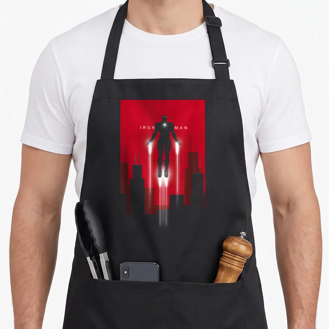 Flight art deco apron - Grey Iron Man silhouette on red background with white text and city skyline — shown on a black cotton canvas apron against a white background
